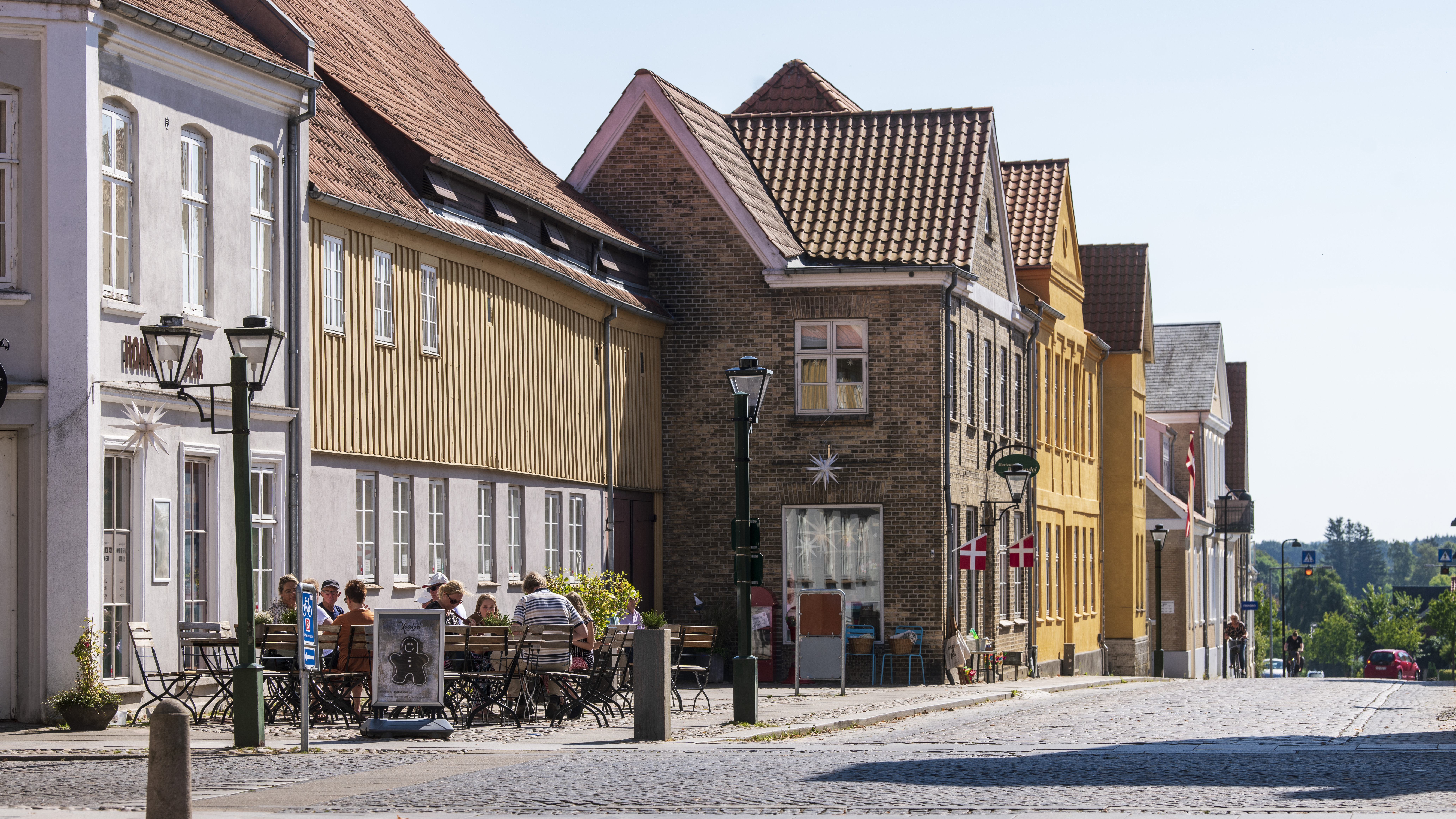People dining outdoors on a cobbled street in Christiansfeld, a UNESCO-listed heritage town in Kolding, Denmark.