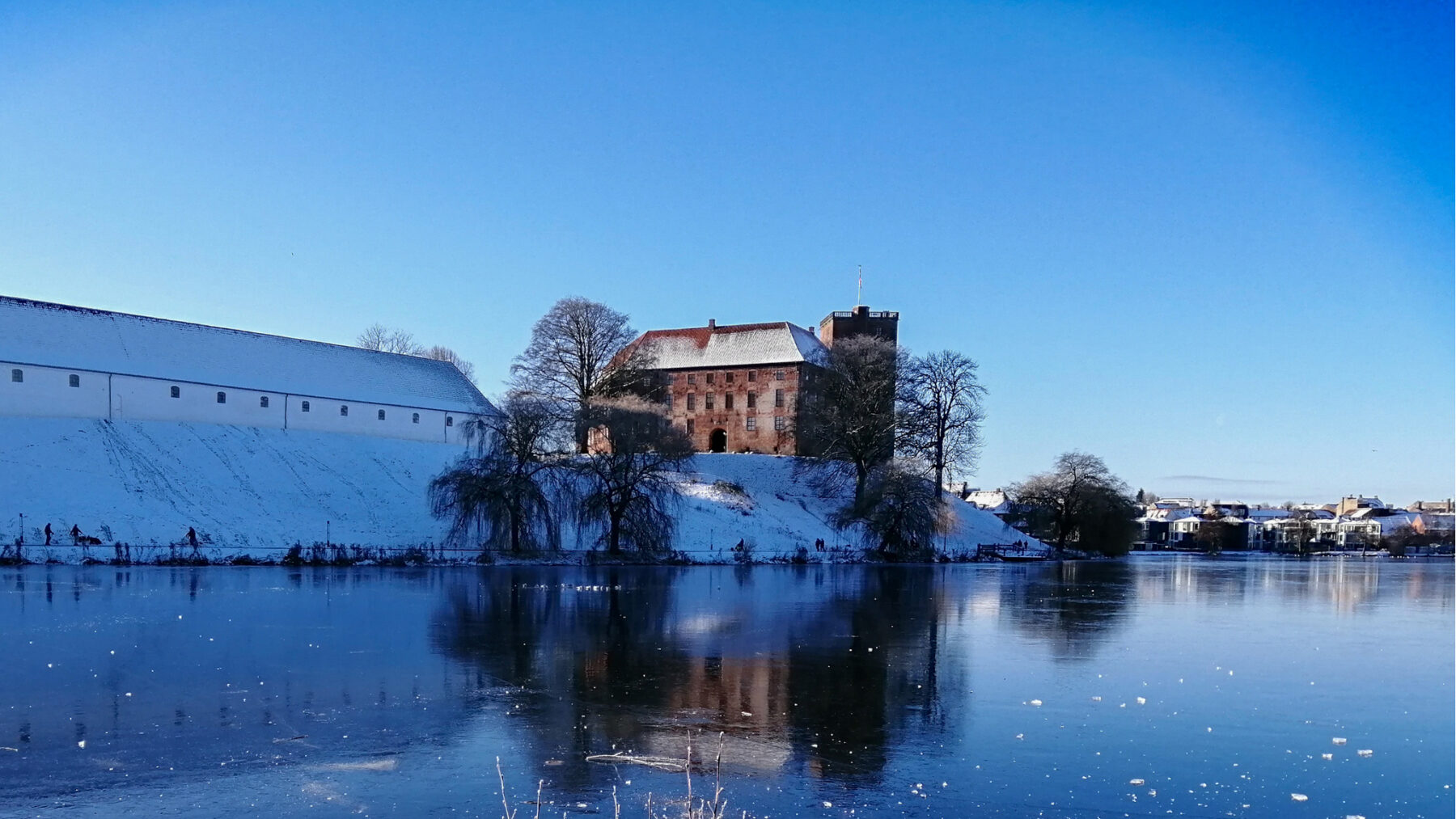 Koldinghus castle in Denmark covered in snow, reflected in the icy lake on a clear winter day