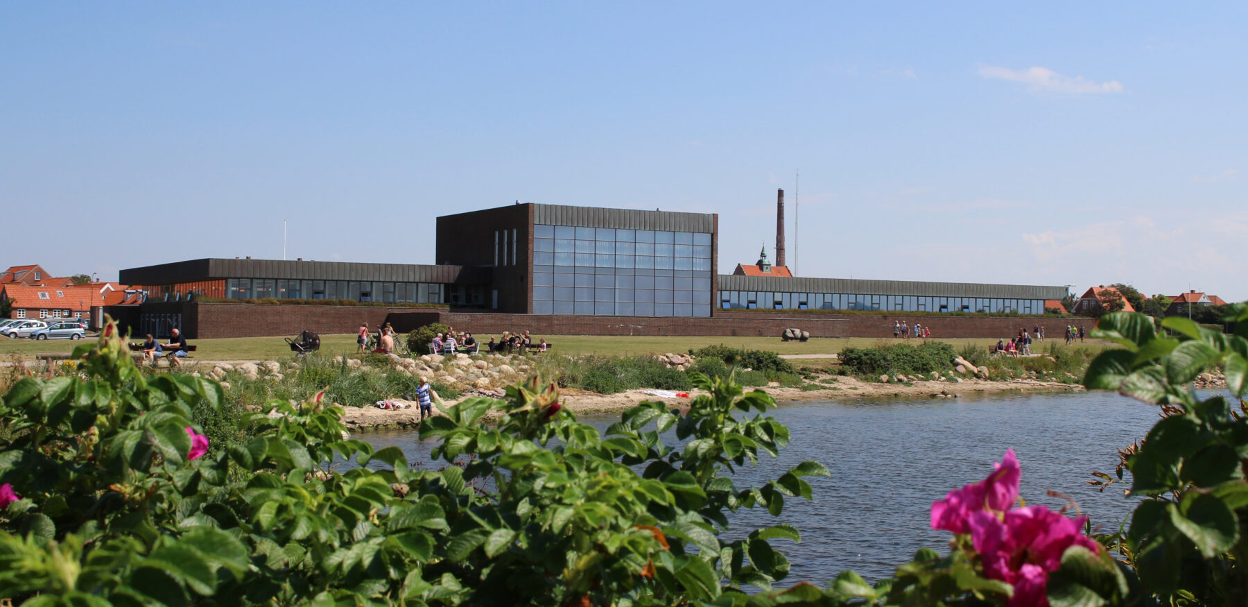 Ringkøbing-Skjern Town Hall viewed from across the lake with flowers in the foreground and people enjoying the sunny weather