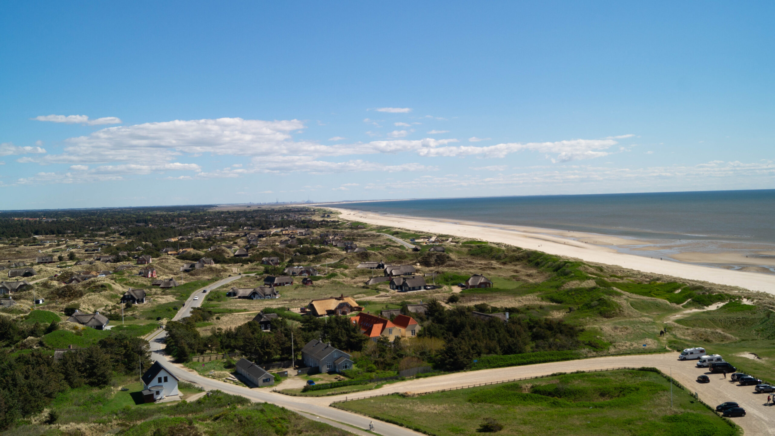 Aerial view of Blåvand, Denmark, showcasing coastal dunes, traditional Danish holiday homes, and the North Sea shoreline on a sunny day.