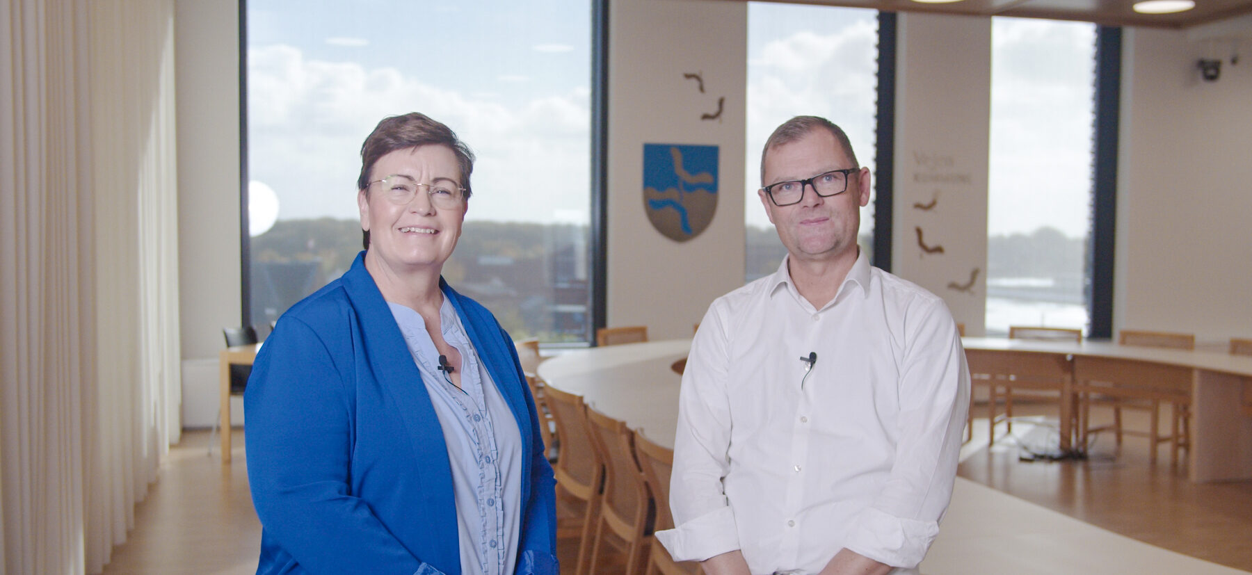 Two professionals standing in a modern meeting room at Vejen Municipality, Denmark, preparing for a business collaboration interview