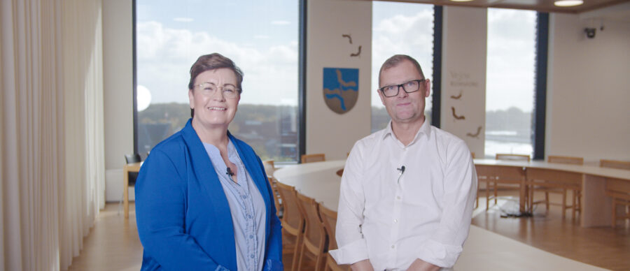 Two professionals standing in a modern meeting room at Vejen Municipality, Denmark, preparing for a business collaboration interview