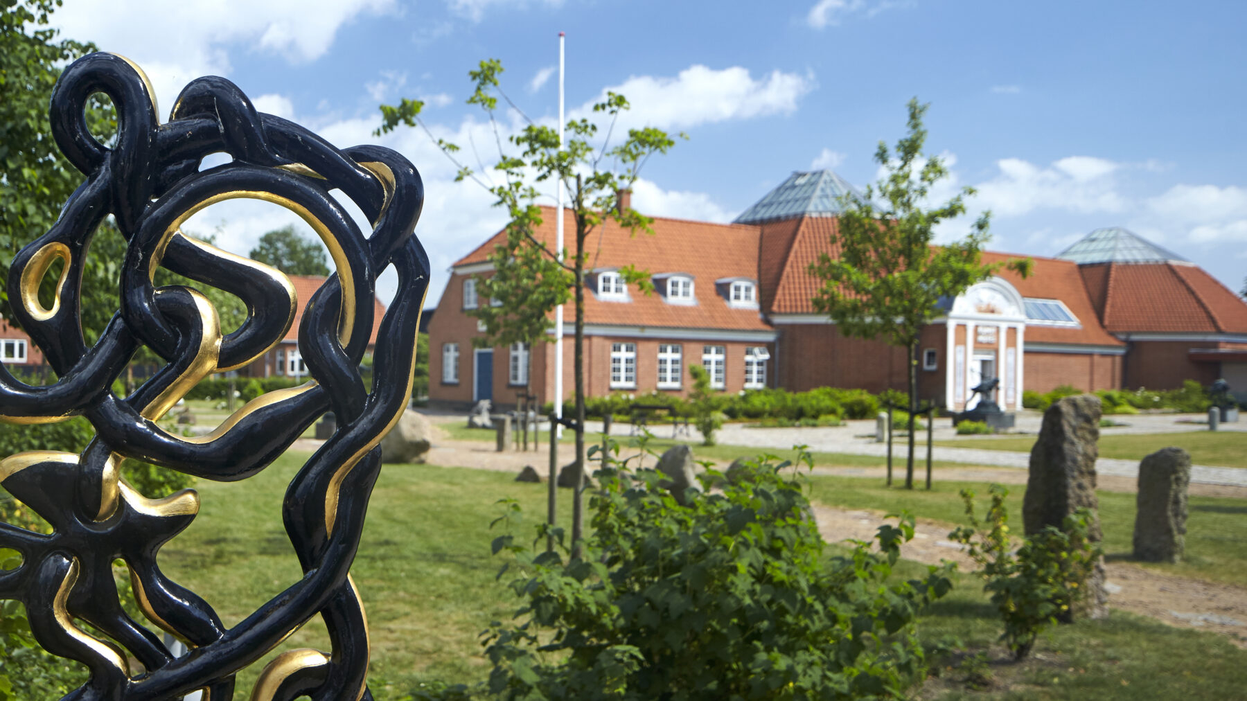 Artistic iron gate by Bjørn Nørgaard at Vejen Art Museum with red brick building in the background