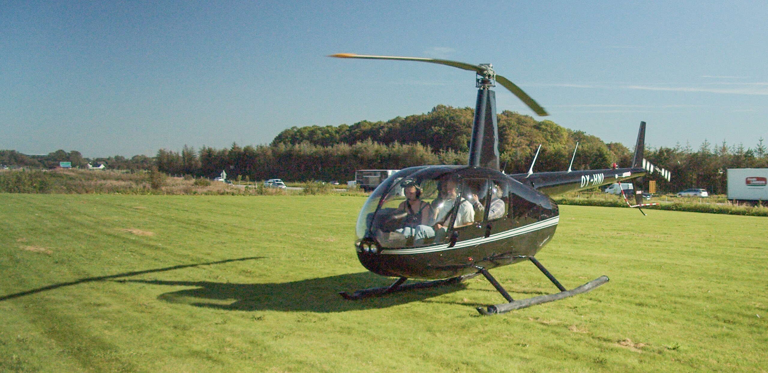 A black helicopter lands on a grassy field during an Intellis event, with passengers visible inside the cockpit.