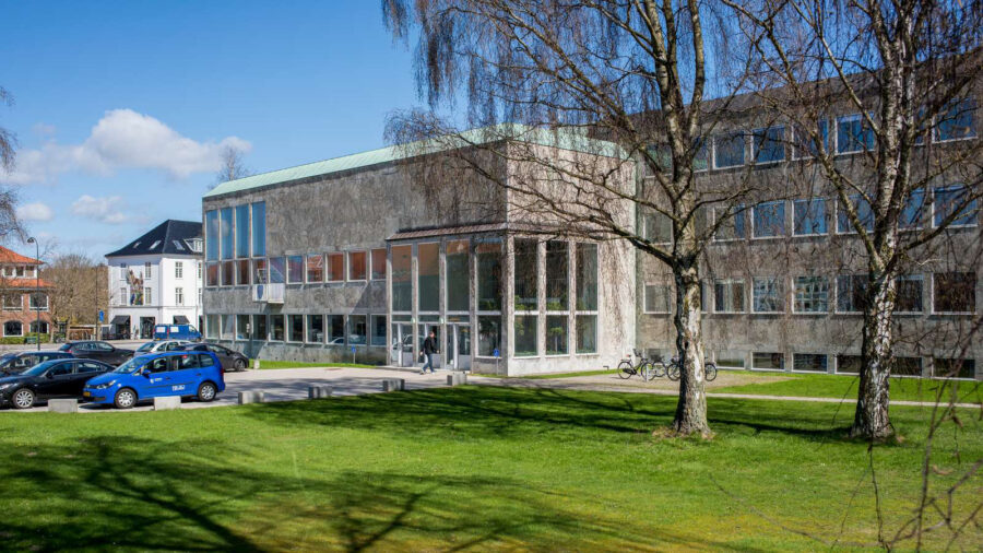 Exterior view of Rudersdal Kommune building on a sunny day, with parked cars and trees casting shadows across a well-maintained lawn.