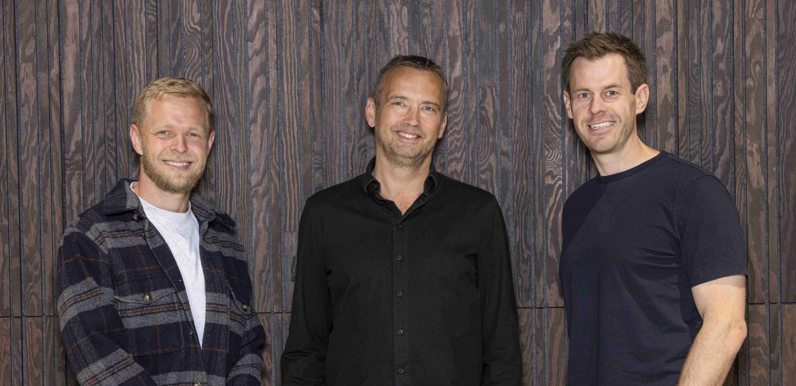 Three members of the Intellis board – Kevin Magnussen, Lars Sneftrup Pedersen and Stig Larsen – standing in front of a dark wooden panel wall, smiling.