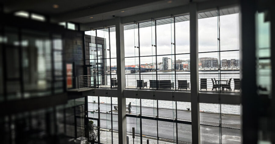 Interior view from Intellis’ Aalborg office showing floor-to-ceiling glass windows overlooking the Limfjord and modern waterfront buildings.