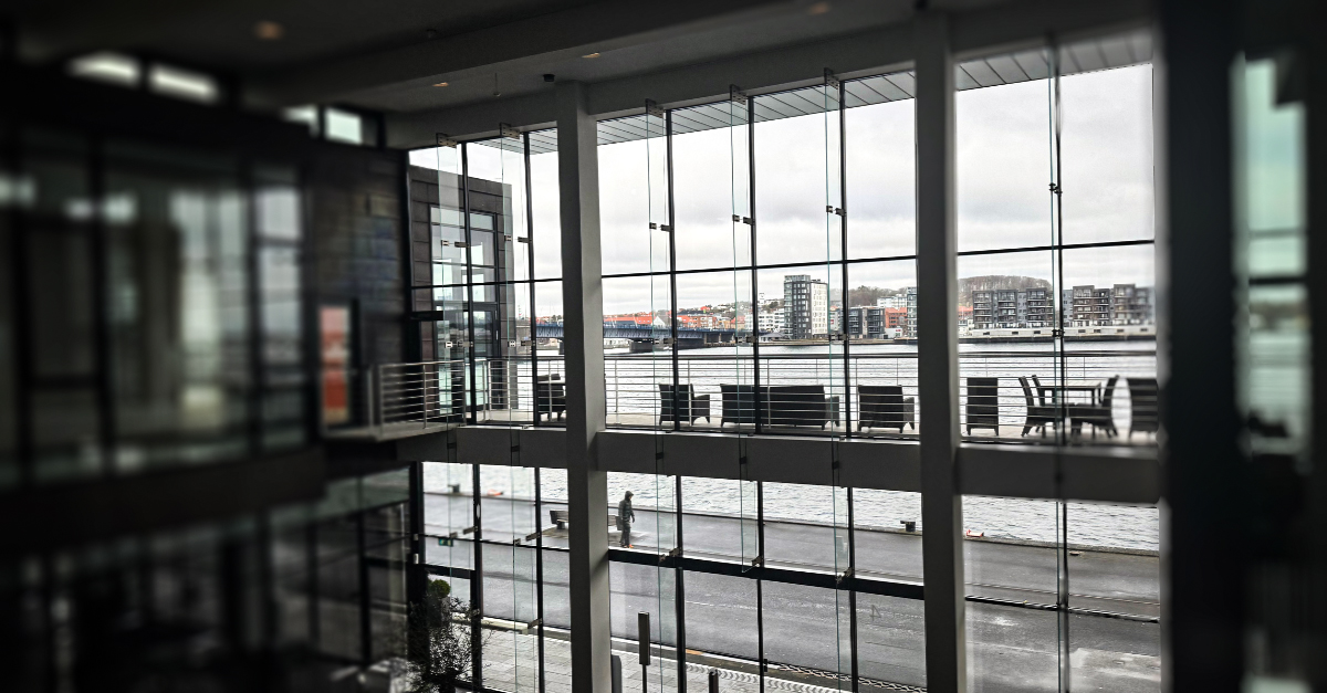 Interior view from Intellis’ Aalborg office showing floor-to-ceiling glass windows overlooking the Limfjord and modern waterfront buildings.