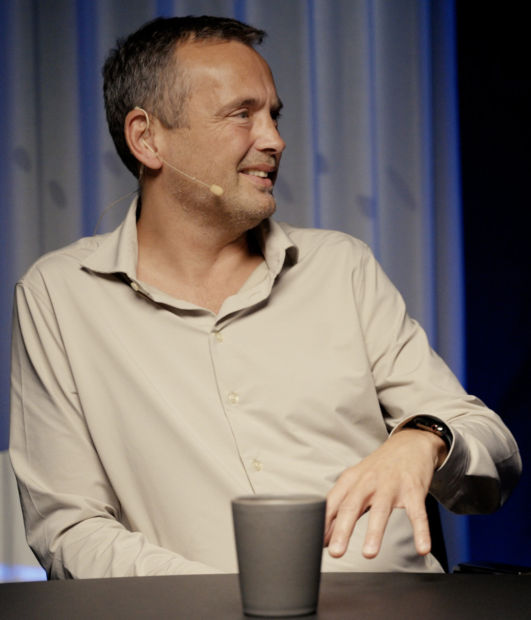 Lars Sneftrup Pedersen speaking during a podcast episode, wearing a headset microphone and light shirt.