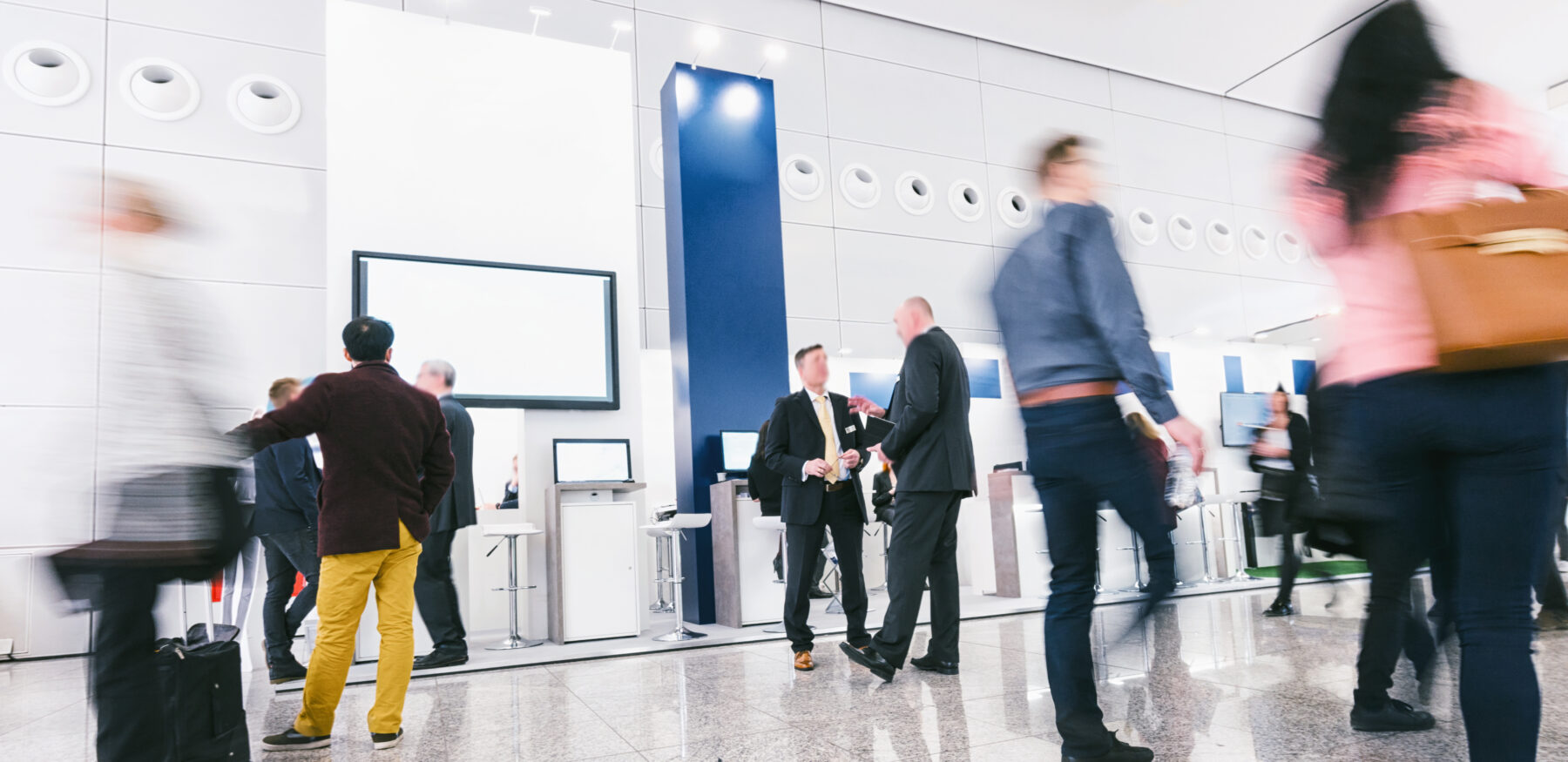 Business professionals networking at a modern corporate event with digital booths and interactive screens.