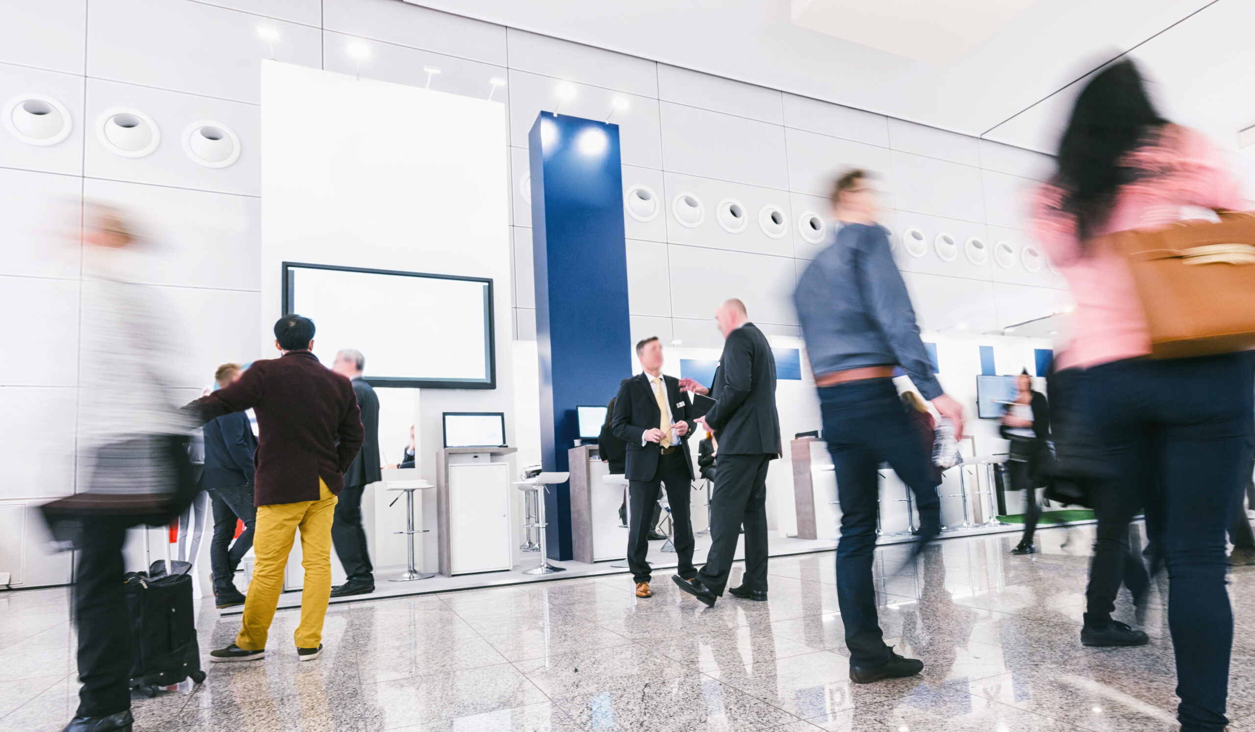 Business professionals networking at a modern corporate event with digital booths and interactive screens.