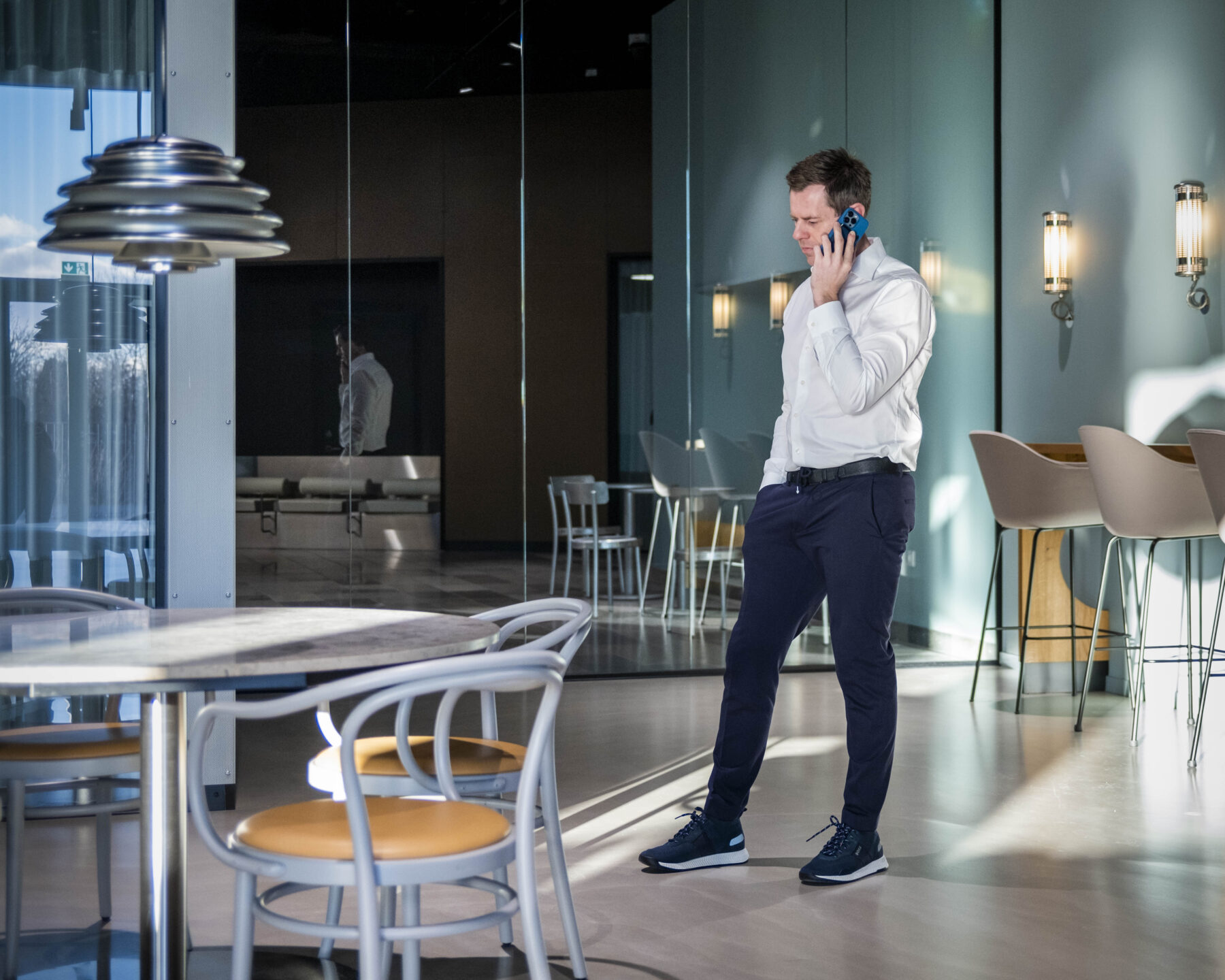 Career man in business casual attire speaking on the phone in a modern office lounge with natural light and contemporary furniture.