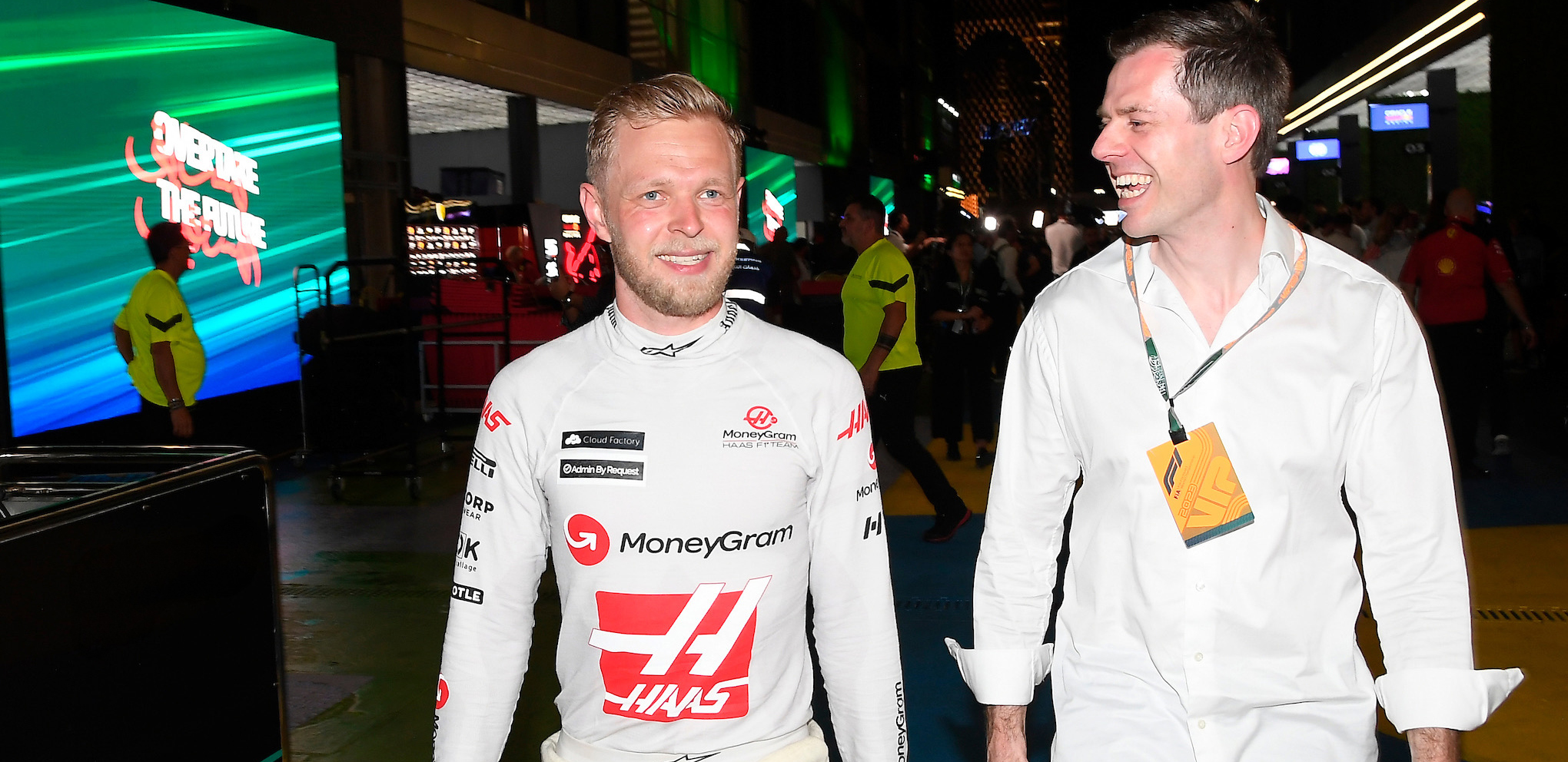 Kevin Magnussen and Stig Larsen smiling after a Formula 1 race event, walking through the paddock.