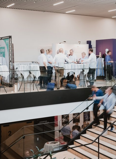 Group of professionals networking around high tables at a business event with people walking downstairs
