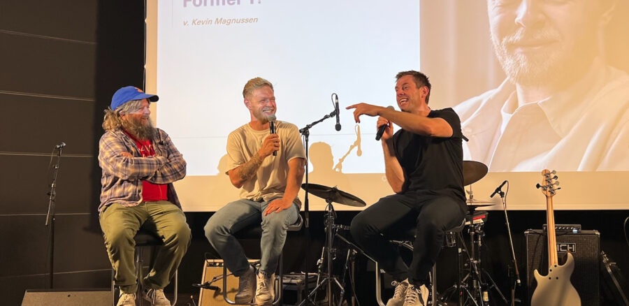 Kevin Magnussen speaks during a lively panel talk at an Intellis event, joined by two other speakers on stage.