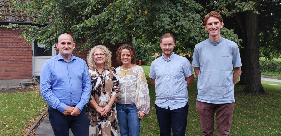 Group photo of Intellis team members with representatives from Fællesindkøb Fyn standing outside in a green, leafy setting.