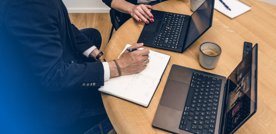 Close-up of a business meeting with laptops, notebooks and coffee cups on a wooden table.