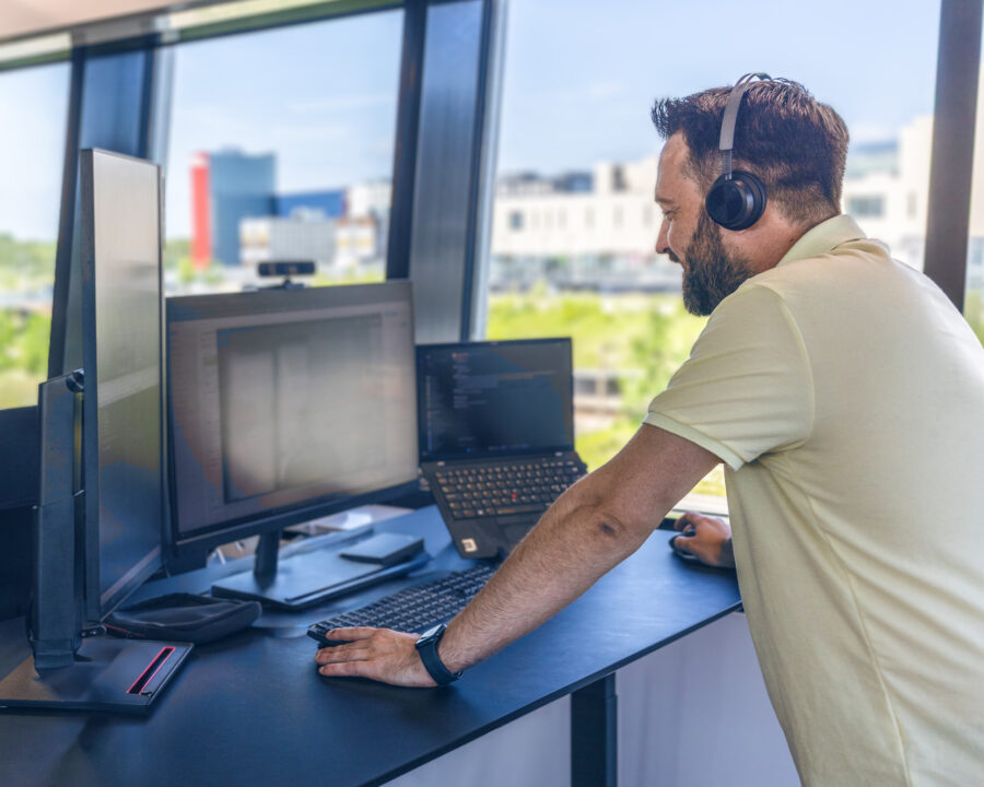 IT professional using dual screens and headset at modern office desk with cityscape in the background