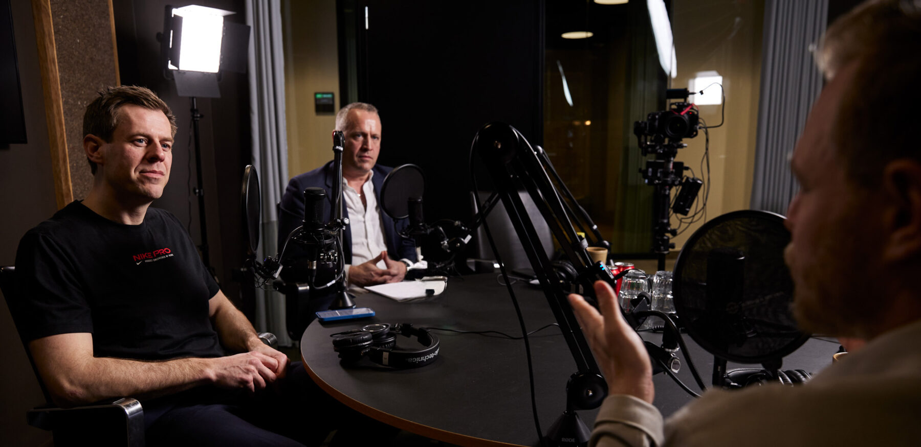 Three men recording a podcast episode in the Intellis studio with lighting and recording equipment
