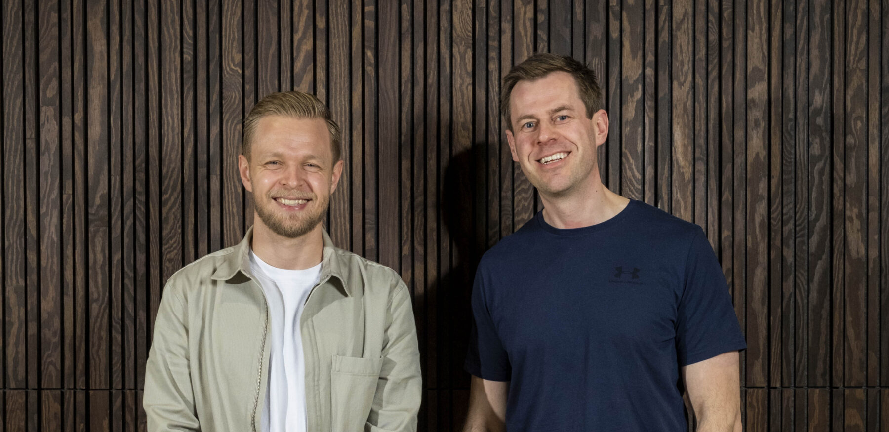 Kevin Magnussen stands smiling with an Intellis team member in front of a dark wood panel wall.
