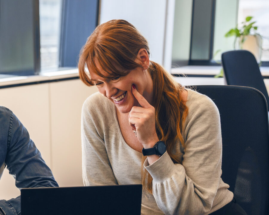 Smiling woman engaging with a colleague during a software demo on a laptop.
