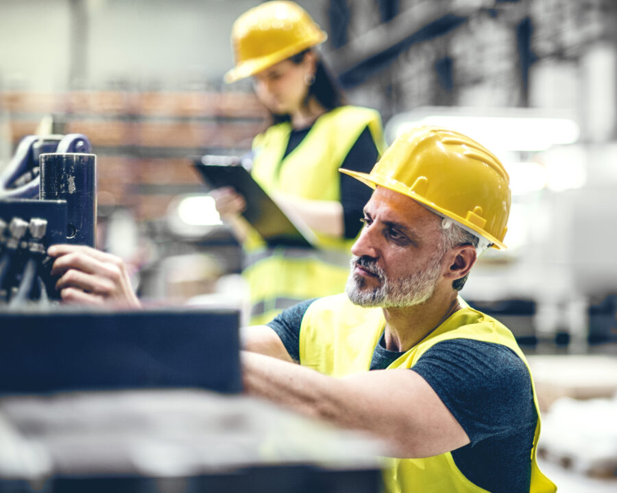 Focused industrial worker adjusting machinery with colleague reviewing data in background.