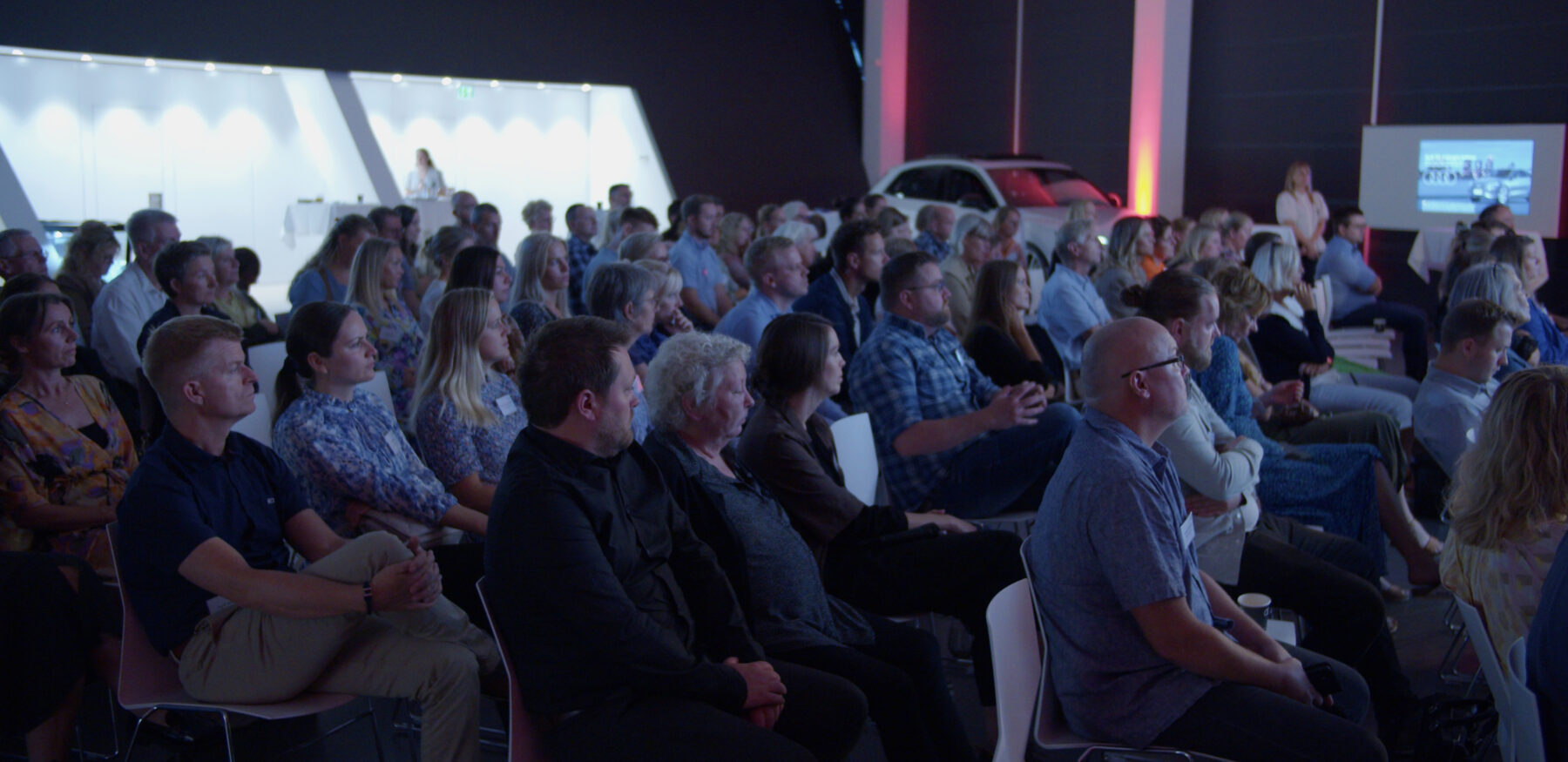 A large audience attentively listens during a professional event hosted by Intellis, seated in a modern, well-lit venue.