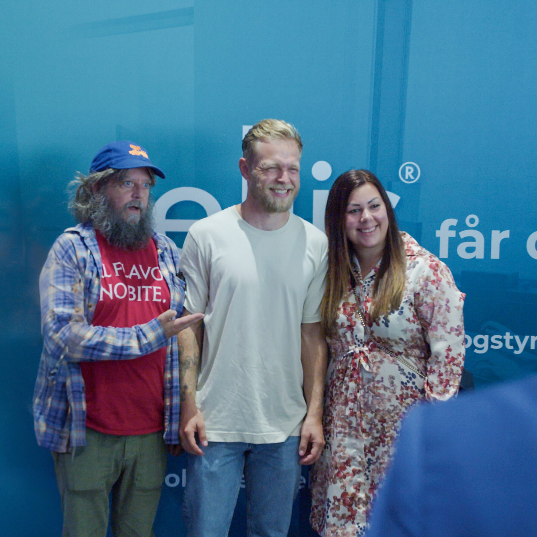 Anders Lund Madsen, Kevin Magnussen, and a smiling client pose for a photo in front of an Intellis-branded wall during one of Intellis' corporate events.