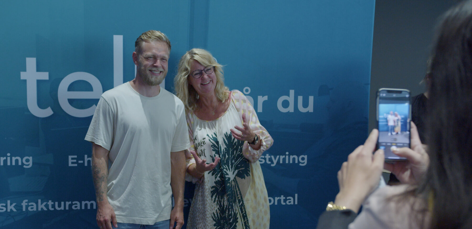 A smiling man and woman pose for a photo during an Intellis event, while someone captures the moment on a smartphone.