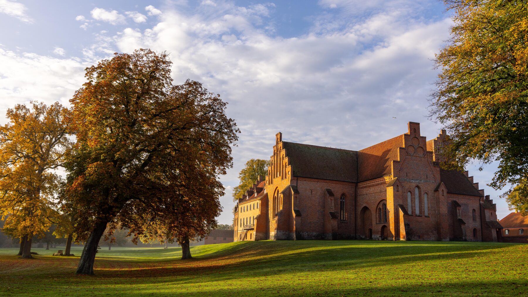 Historic Herlufsholm School in Næstved Municipality, Denmark, surrounded by autumn trees under a partly cloudy sky