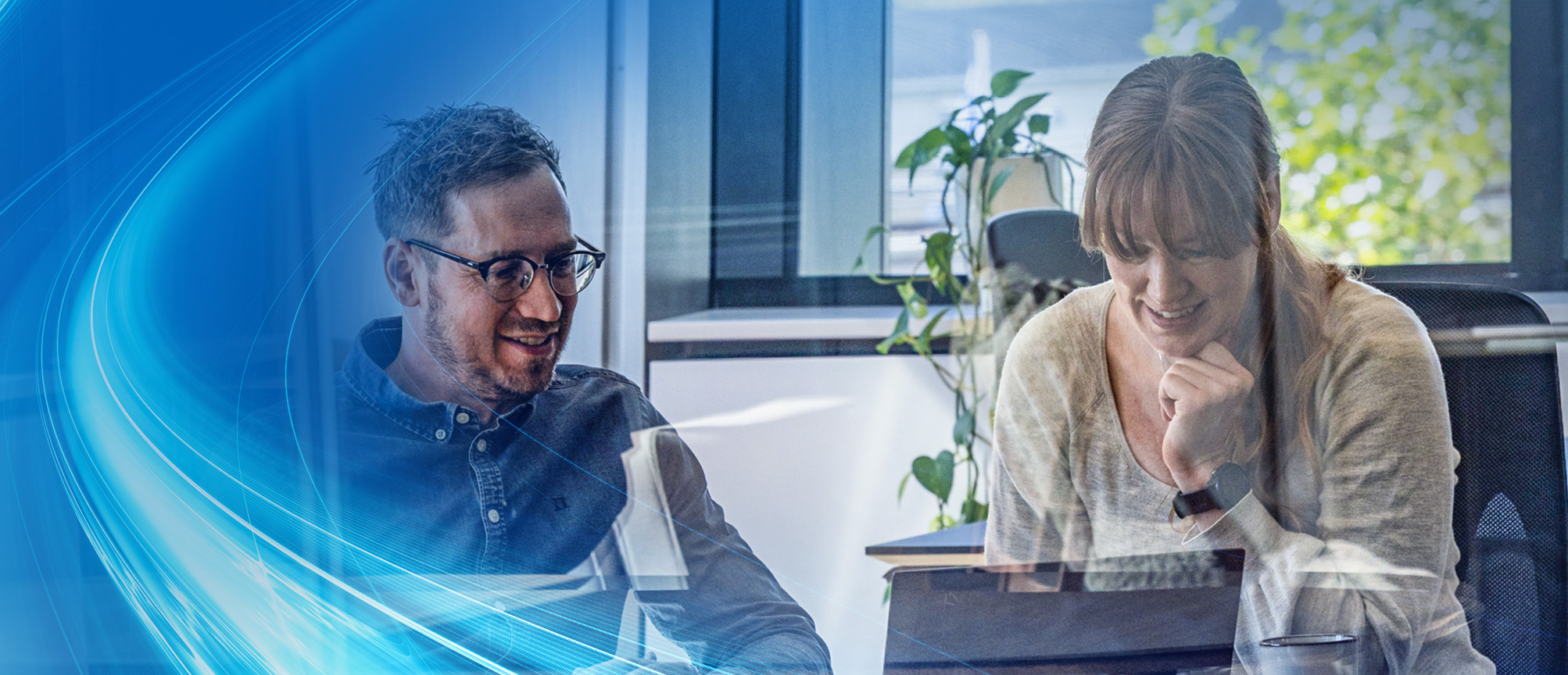 Two colleagues collaborating in a modern office, smiling while discussing a project on a laptop, with a blue digital wave overlay.