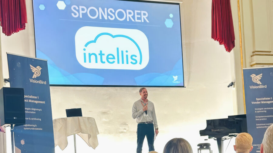 Intellis shown as sponsor on stage at a VisionBird vendor management event with a speaker presenting to an audience.